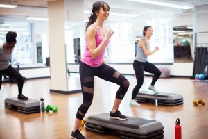 Smiling confident female athletes exercising on aerobics steps in gym