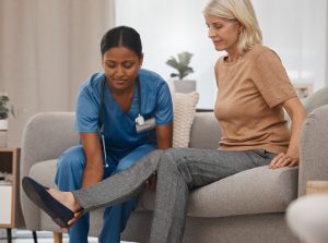 Foot, nurse or senior woman with physical therapy for injury, rehabilitation massage and healthcare worker help with pain. Elderly patient, doctor and physio therapist or medical expert on sofa